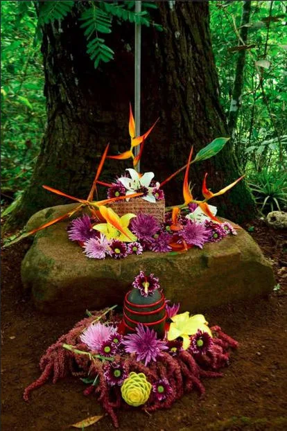 Colorful flowers, ritual object on large rock in front of tree in the tropics.