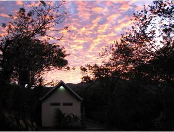 Early morning, colorful sunrise with small house in foreground, tree silhouettes.