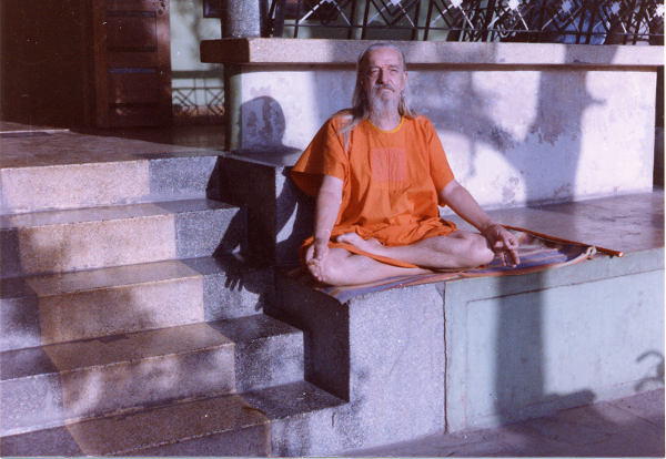 Mahendranath sitting on porch in meditative pose wearing orange robe.